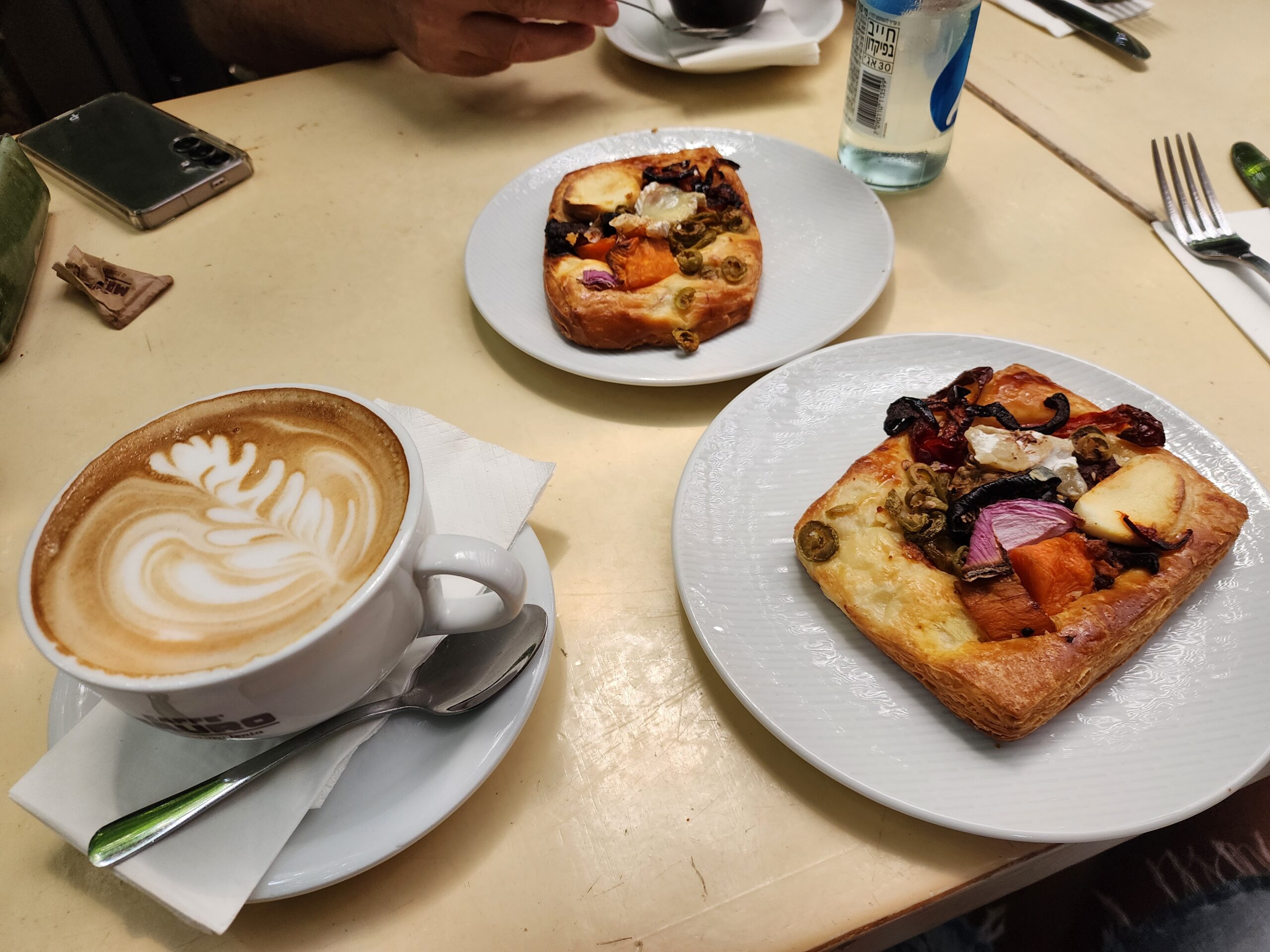 Cappuccino with rosetta latte art beside two puff pastry tarts topped with roasted vegetables